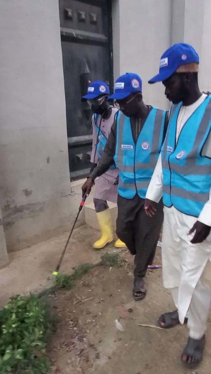 Members of the Dorayi programme team operating a sprayer outside a building.